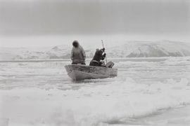 two people in boat spear fishing in icy water